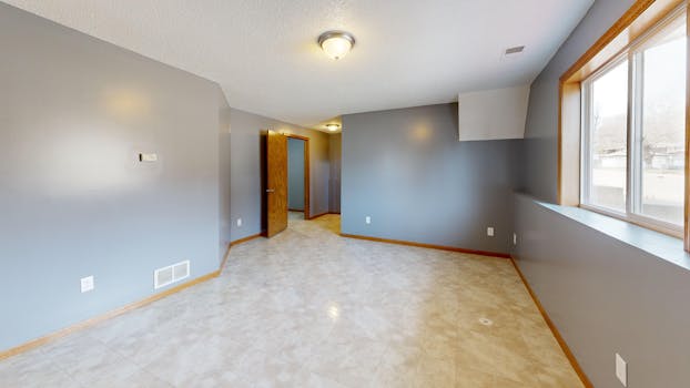 Spacious empty room with grey walls, large window, and wood trim, perfect for real estate listings.