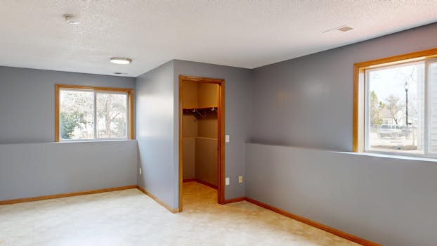 Bright empty room with large windows and walk-in closet featuring gray walls and wooden trims.