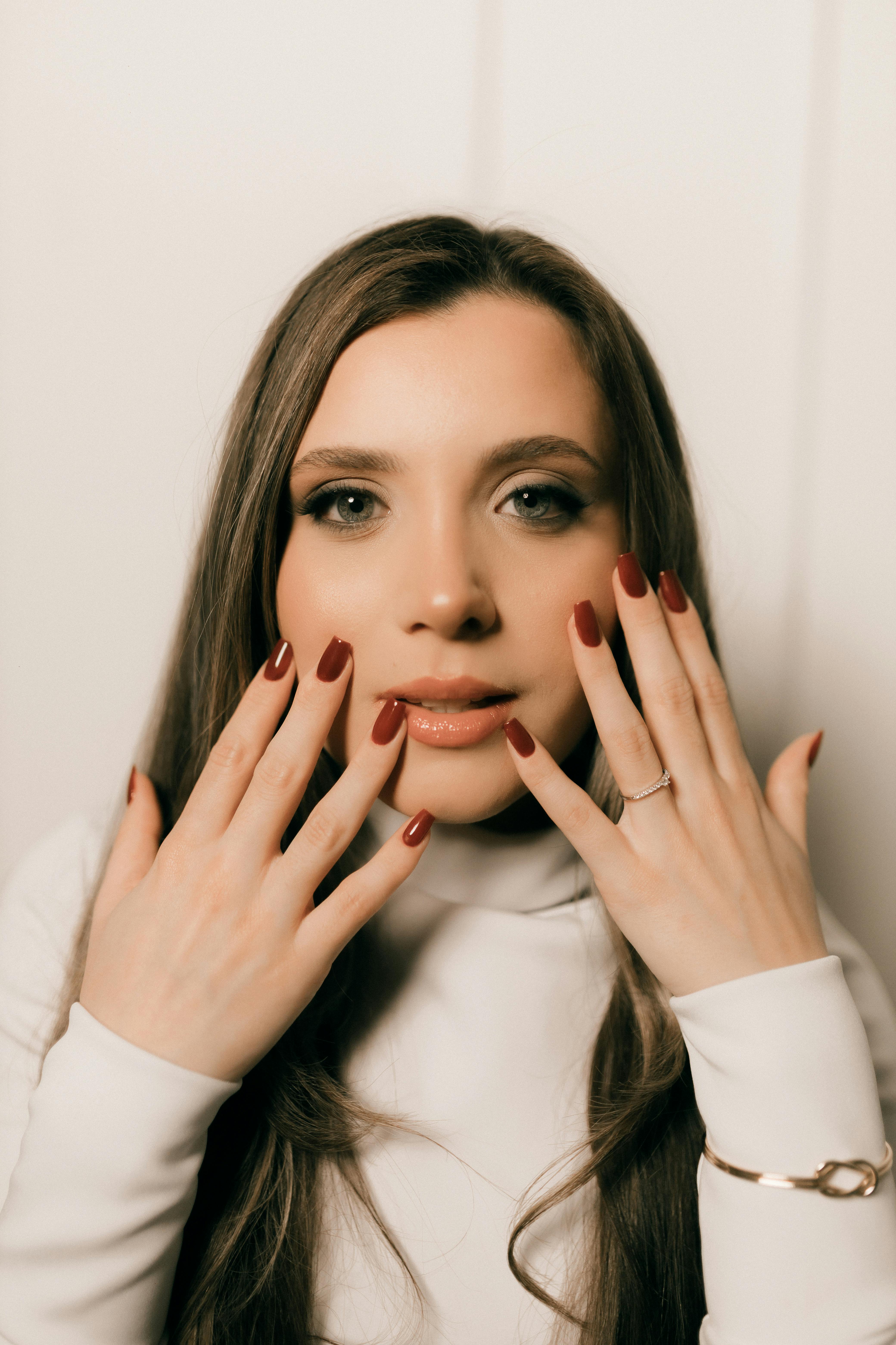 bezplatná Detailní portrét ženy s elegantní červenou manikúrou v jemném, moderním prostředí. Základová fotografie