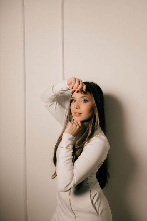 Free Stylish woman poses gracefully in a white outfit against a neutral background. Stock Photo