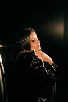 A woman in a glamorous outfit strikes a pose with dramatic lighting in a dark setting.
