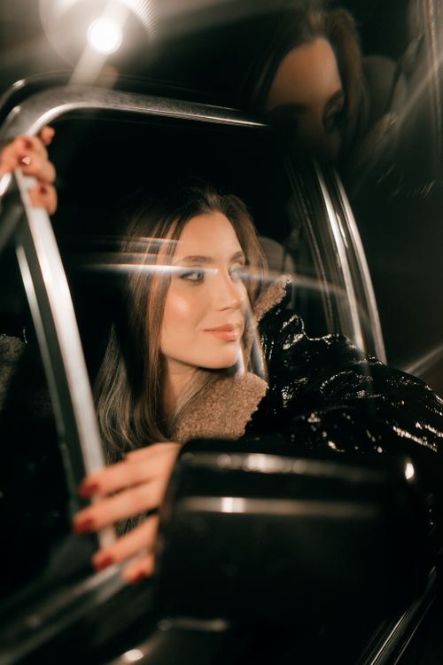 Free A fashionable woman looks out from a car window at night, exuding glamour and elegance. Stock Photo