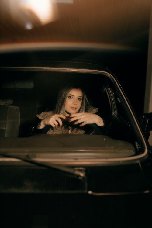 Free A young woman seated in a car at night, hands on the wheel, with a calm expression. Stock Photo