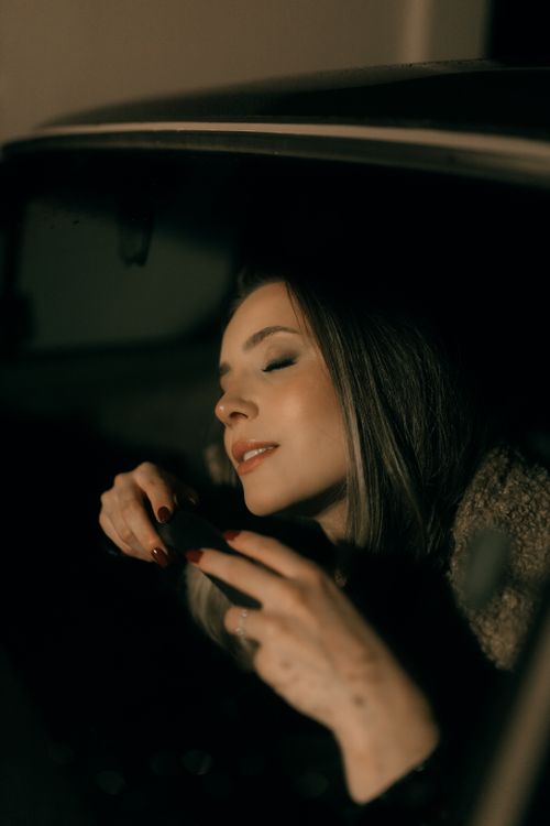 Free Woman with closed eyes in a car enjoying a serene moment at night. Stock Photo
