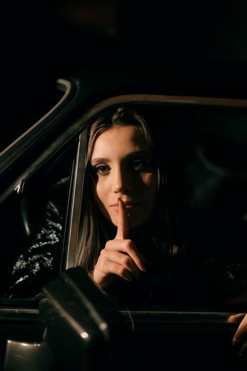 Free A captivating portrait of a woman in a car at night, suggesting silence with a finger on her lips. Stock Photo