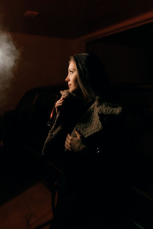 Free Moody portrait of a woman in a coat exhaling smoke, captured at night with dramatic lighting. Stock Photo