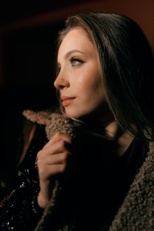 Free Warm portrait of a young woman in a cozy coat with soft lighting and thoughtful expression. Stock Photo