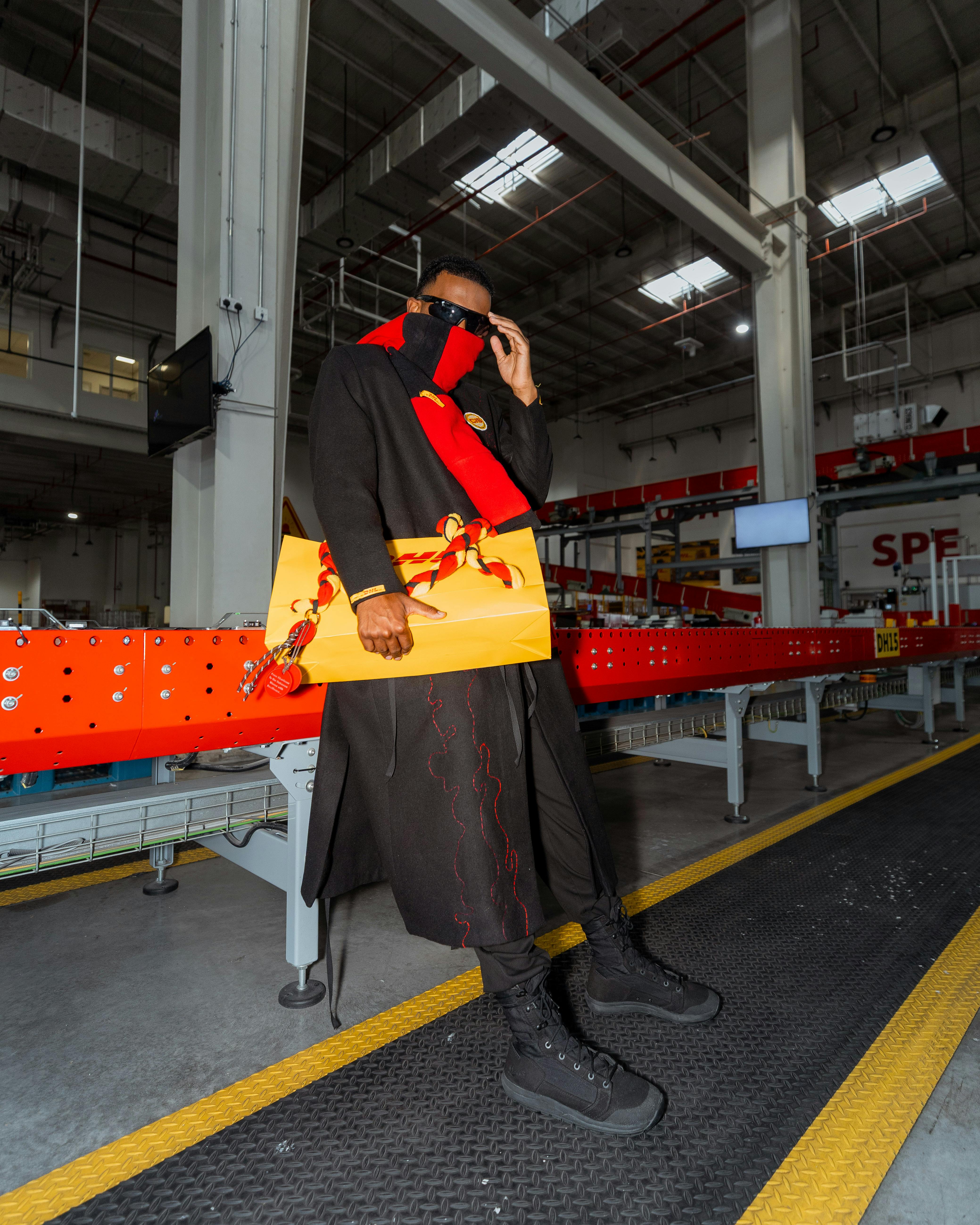 Gratis Mann i elegant antrekk som holder røde og gule gjenstander i et moderne industrimiljø. Arkivbilde