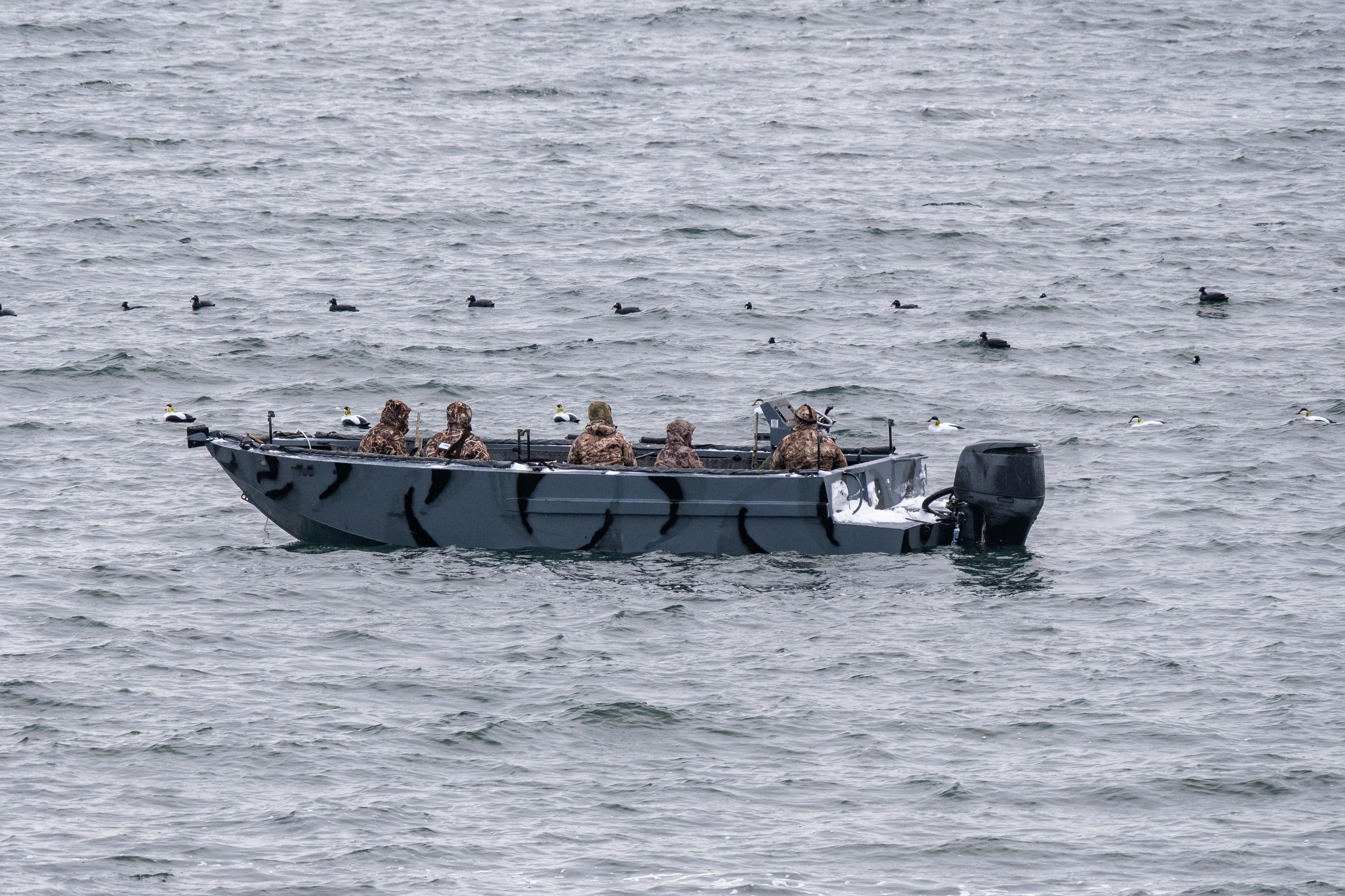 Hunters on a boat in Jamestown, Rhode Island, engage in duck hunting amidst Atlantic Ocean waves.