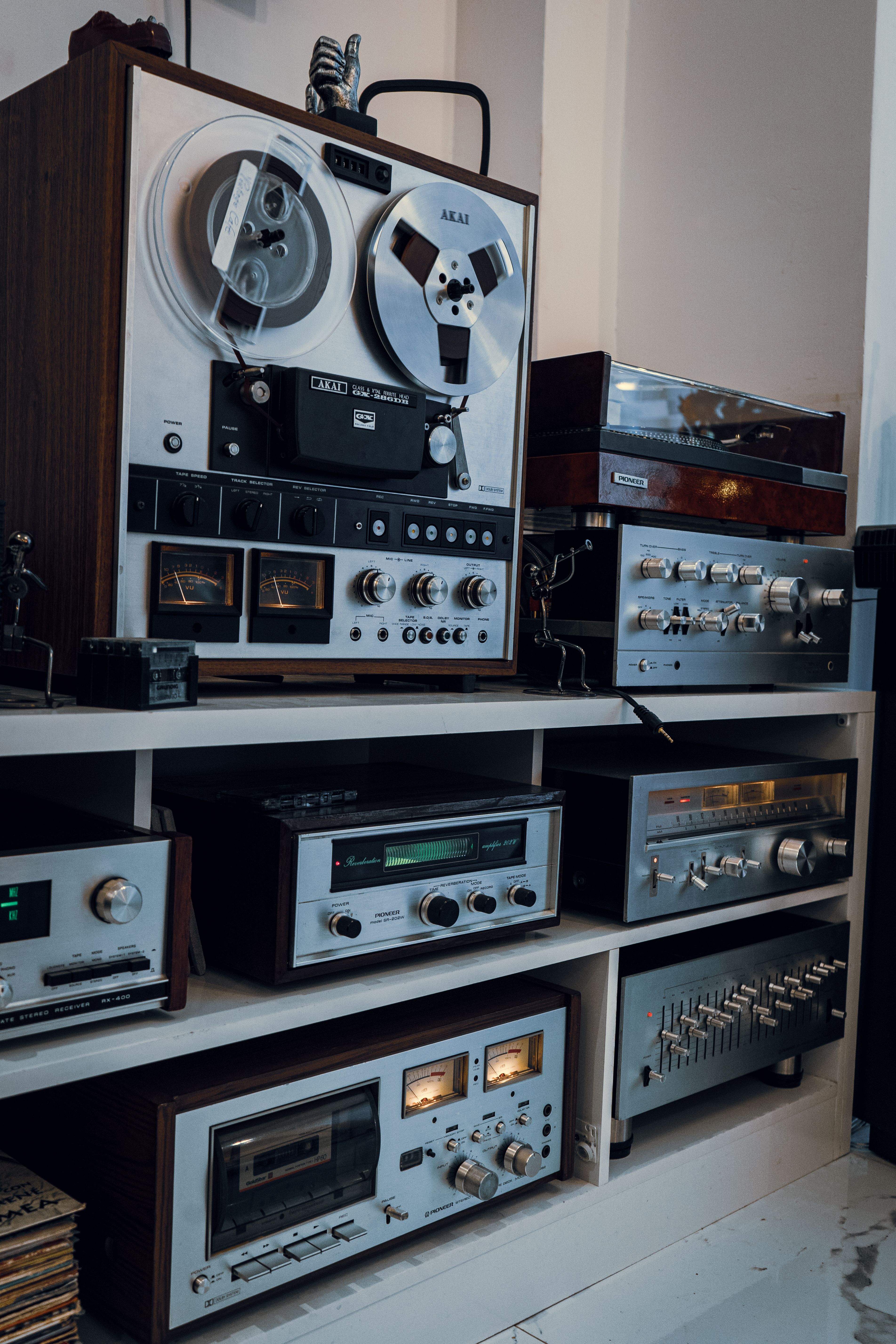 A collection of vintage audio equipment including tape recorders and amplifiers on a white shelf indoors.