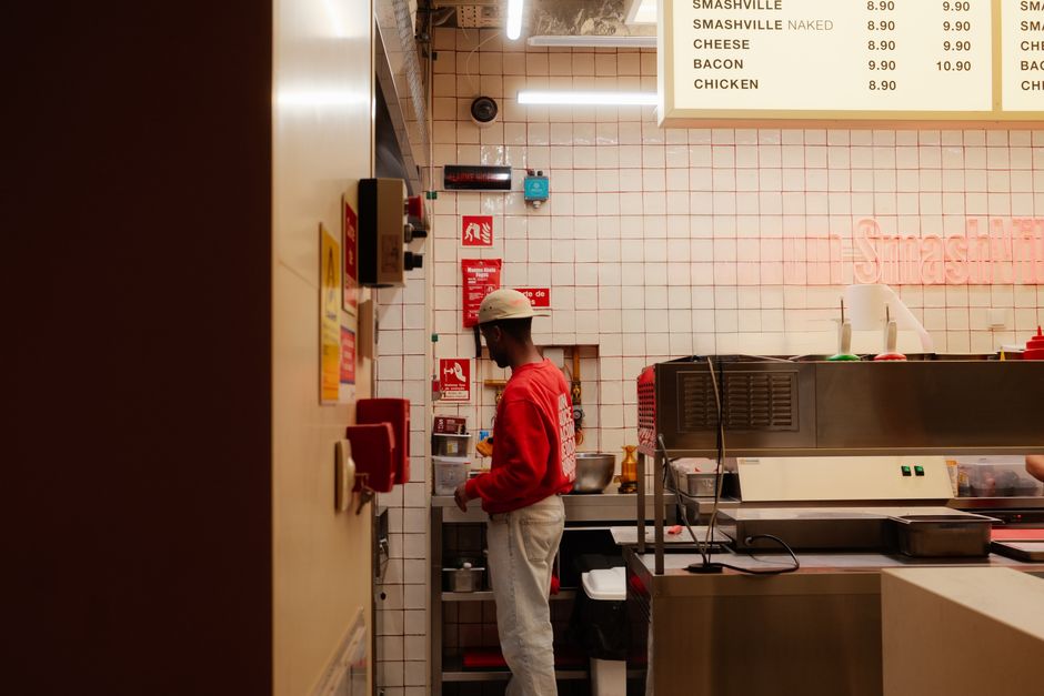 Chef working in a Lisbon diner kitchen, preparing burgers with a menu sign overhead.