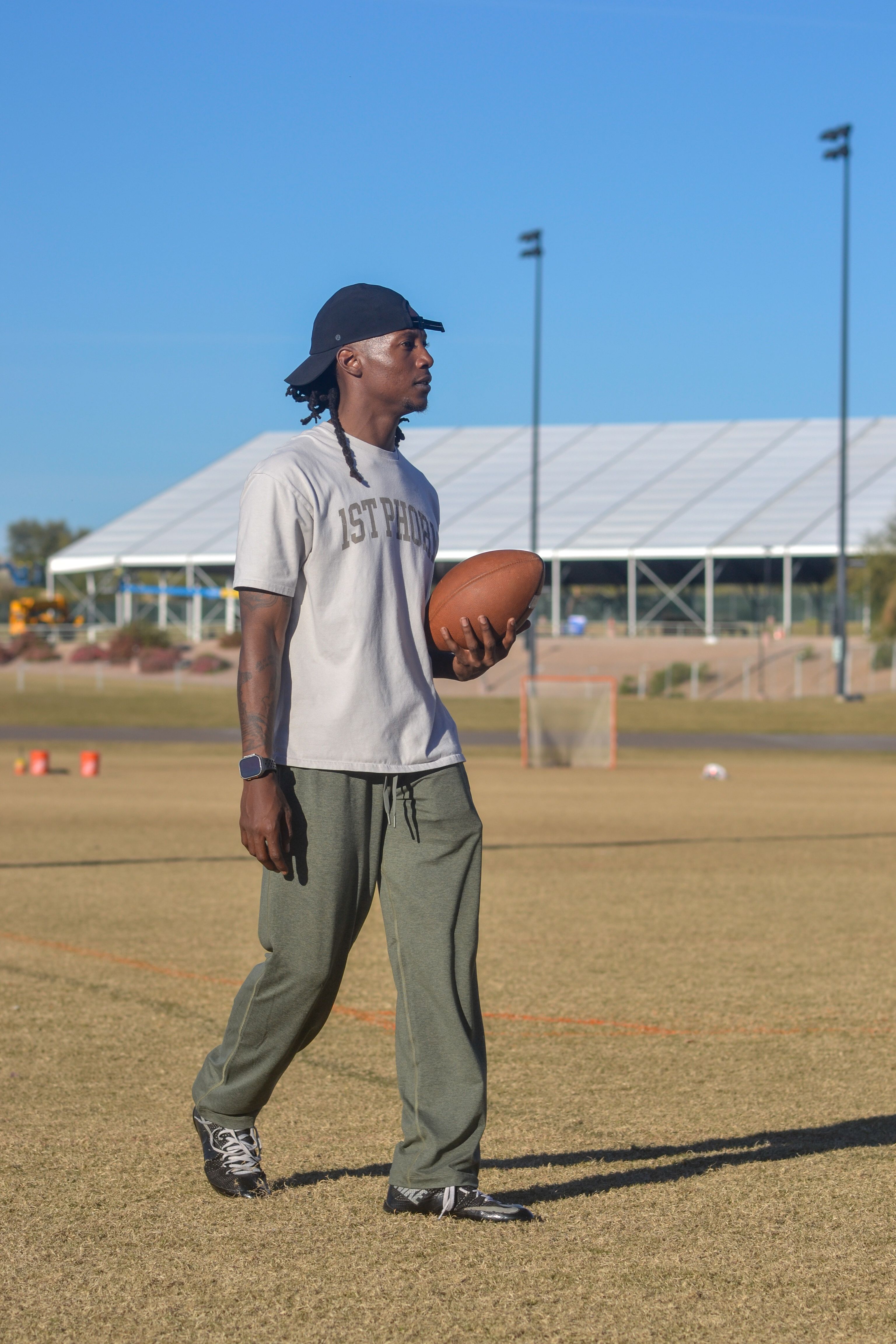 Teenager holding a football on a practice field in Scottsdale, Arizona, under a clear blue sky.
