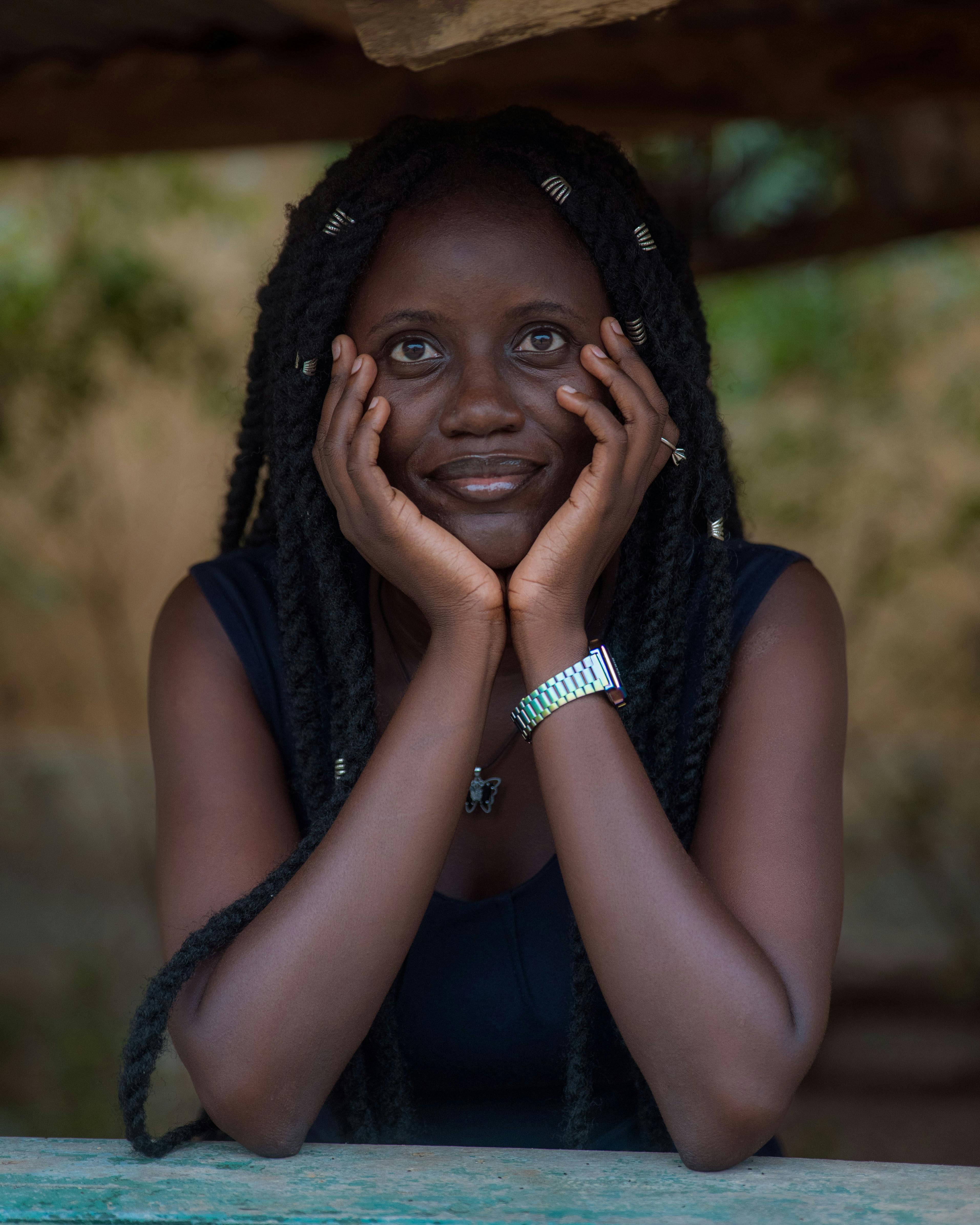 Charming portrait of a young woman with long dreadlocks smiling thoughtfully outdoors.