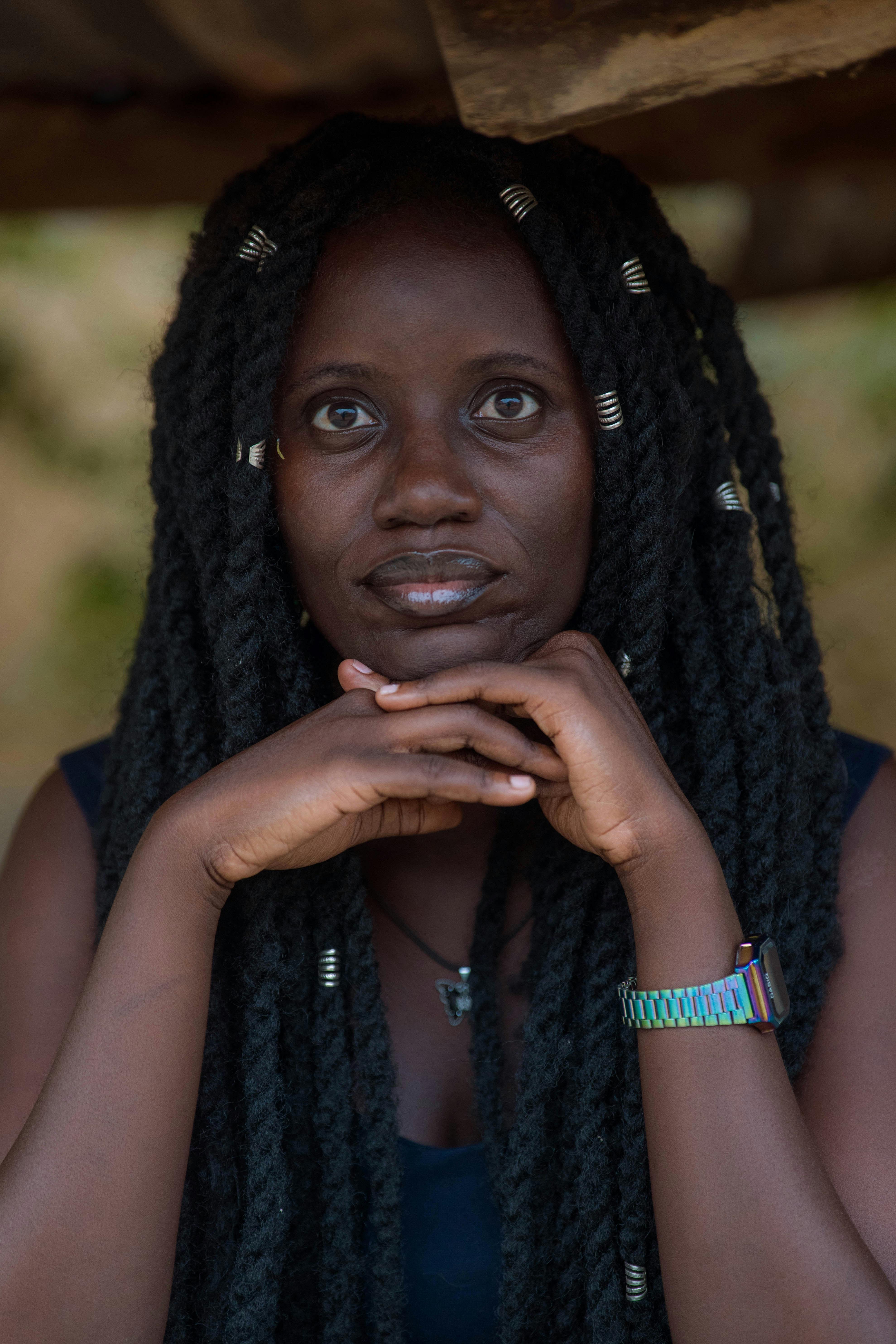 Gratis Nærbilde av en kvinne med langt flettet hår og fargerik klokke, plassert i et naturlig utendørsmiljø. Arkivbilde