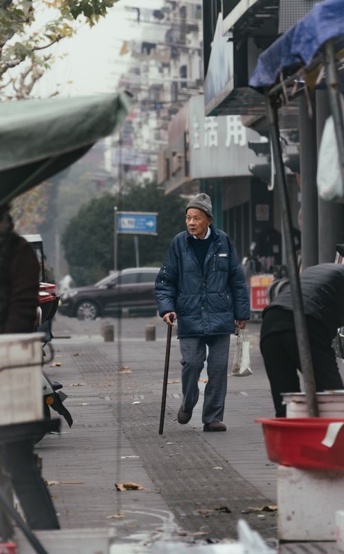 Free Senior man walks down a city street using a cane, capturing a moment of daily life. Stock Photo
