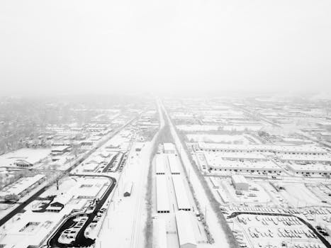 Aerial view of a snow-covered city landscape during winter, showcasing roads and buildings.