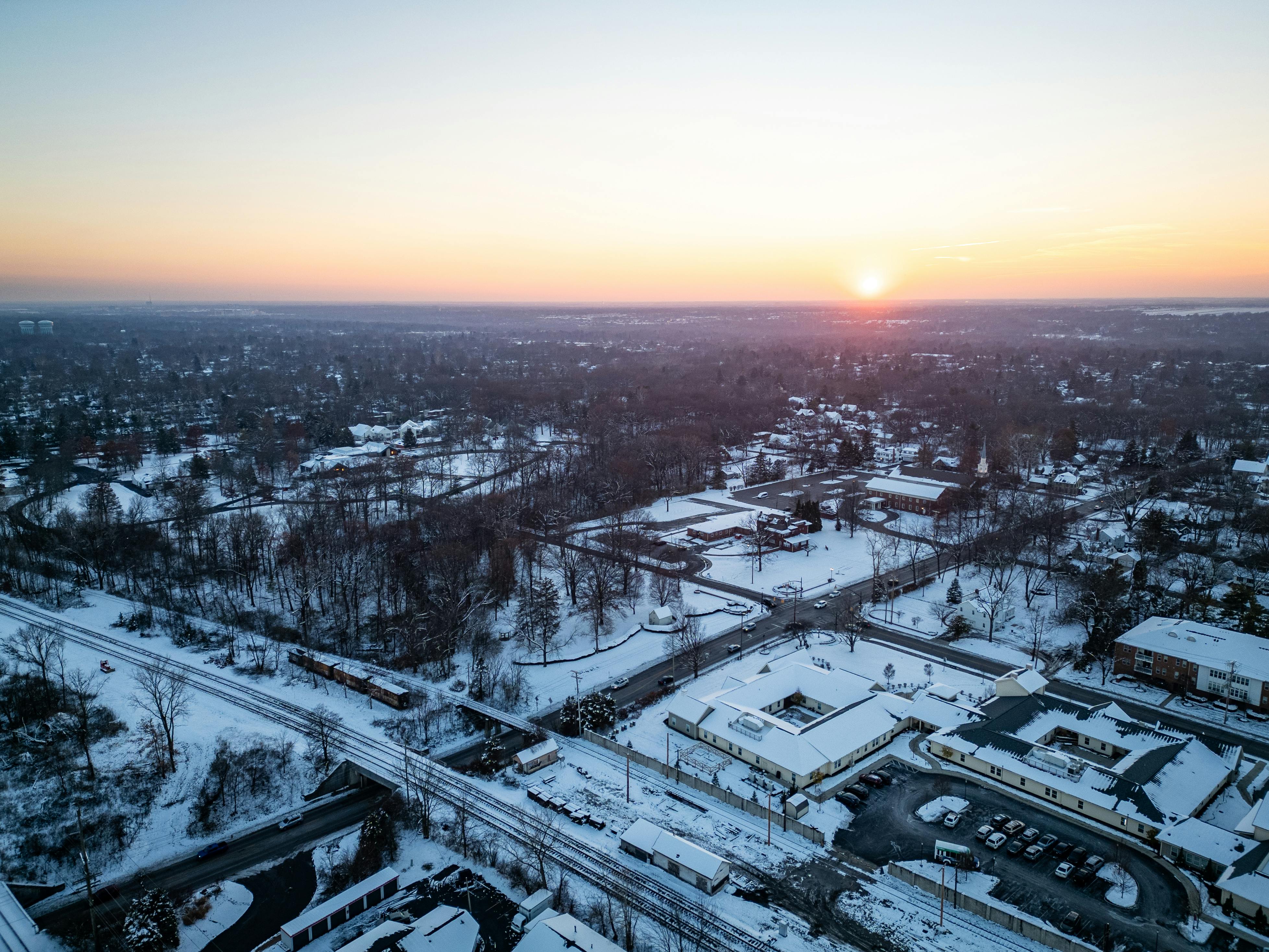 A serene aerial view of a snow-covered suburban town under a tranquil sunrise sky.