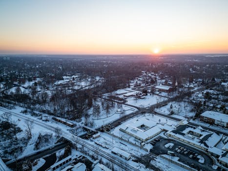 A serene aerial view of a snow-covered suburban town under a tranquil sunrise sky.