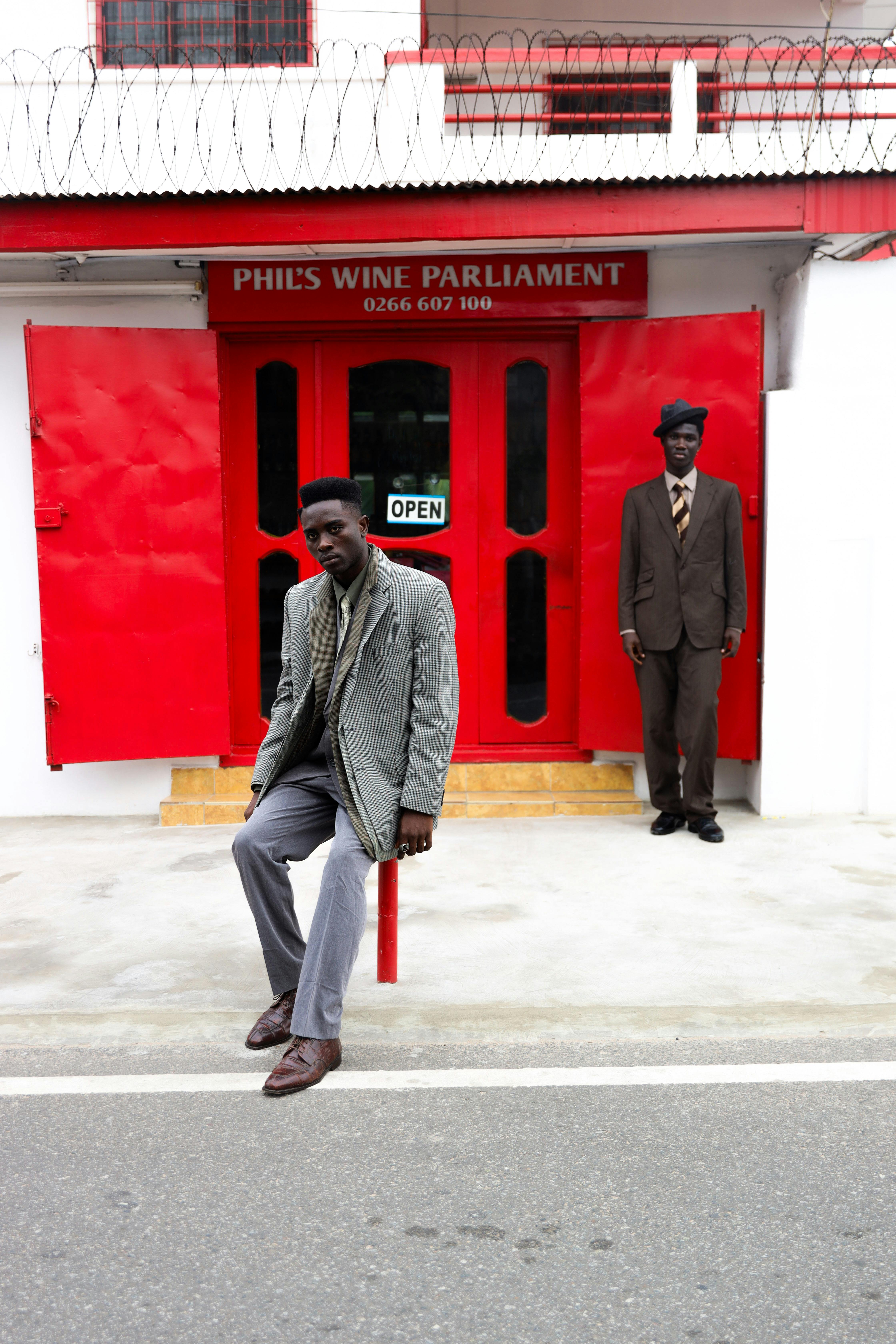 De franc Dos homes amb vestit posen davant d'una botiga vermella vibrant per a una elegant foto urbana. Foto d'estoc