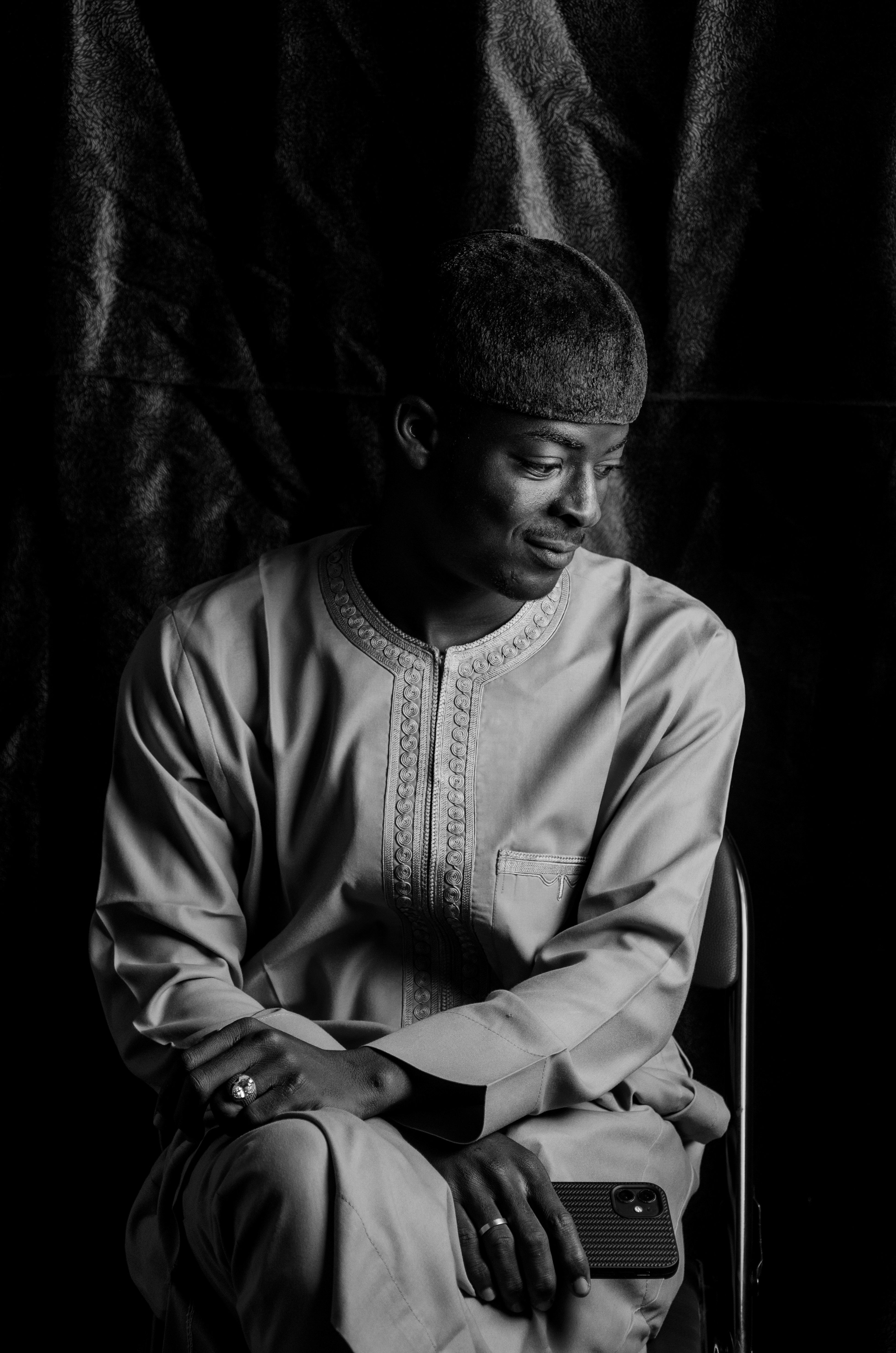 Black and white portrait of a man in traditional Nigerian attire seated thoughtfully.
