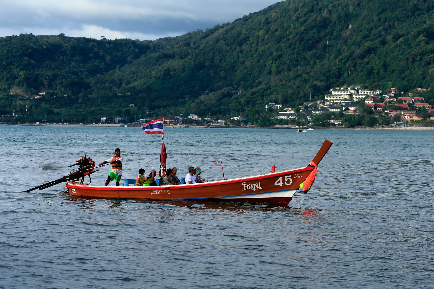 Travelers crossing Phuket waters in a small Thai-flagged traditional longtail boat