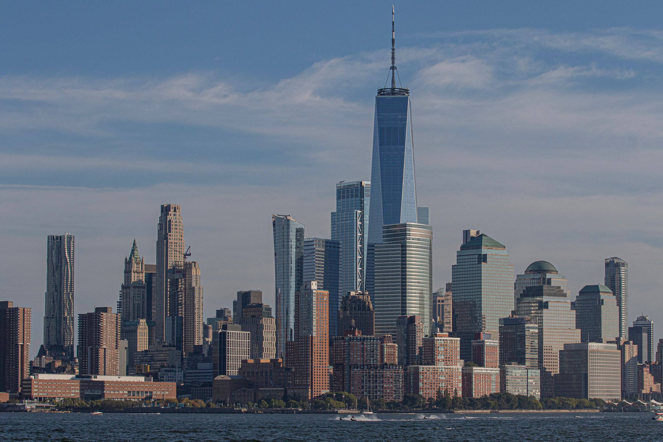 Breathtaking view of Lower Manhattan under a bright blue sky, featuring the iconic One World Trade Center.