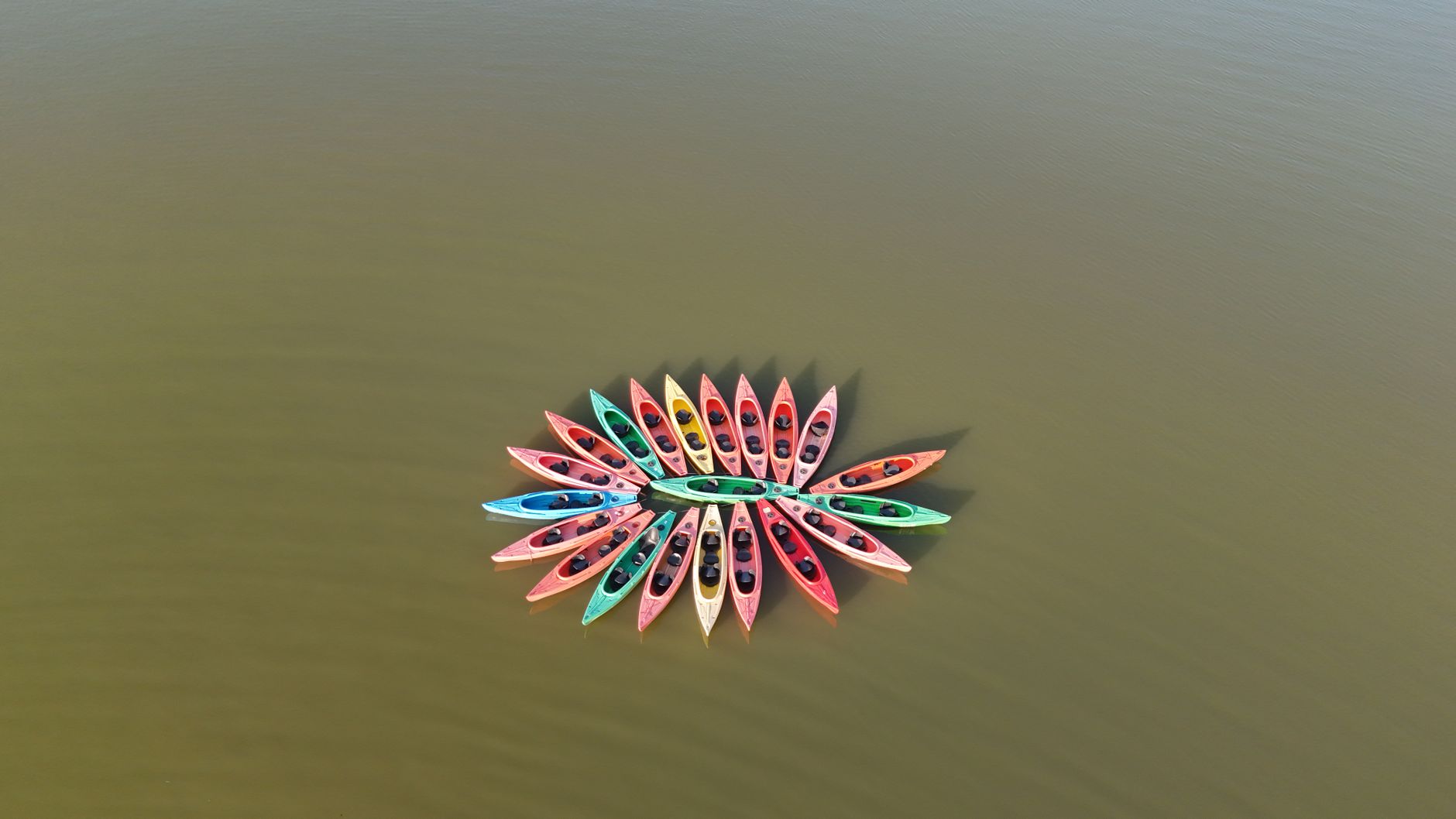 Drone view of multicolored kayaks forming a circle on calm lake waters.