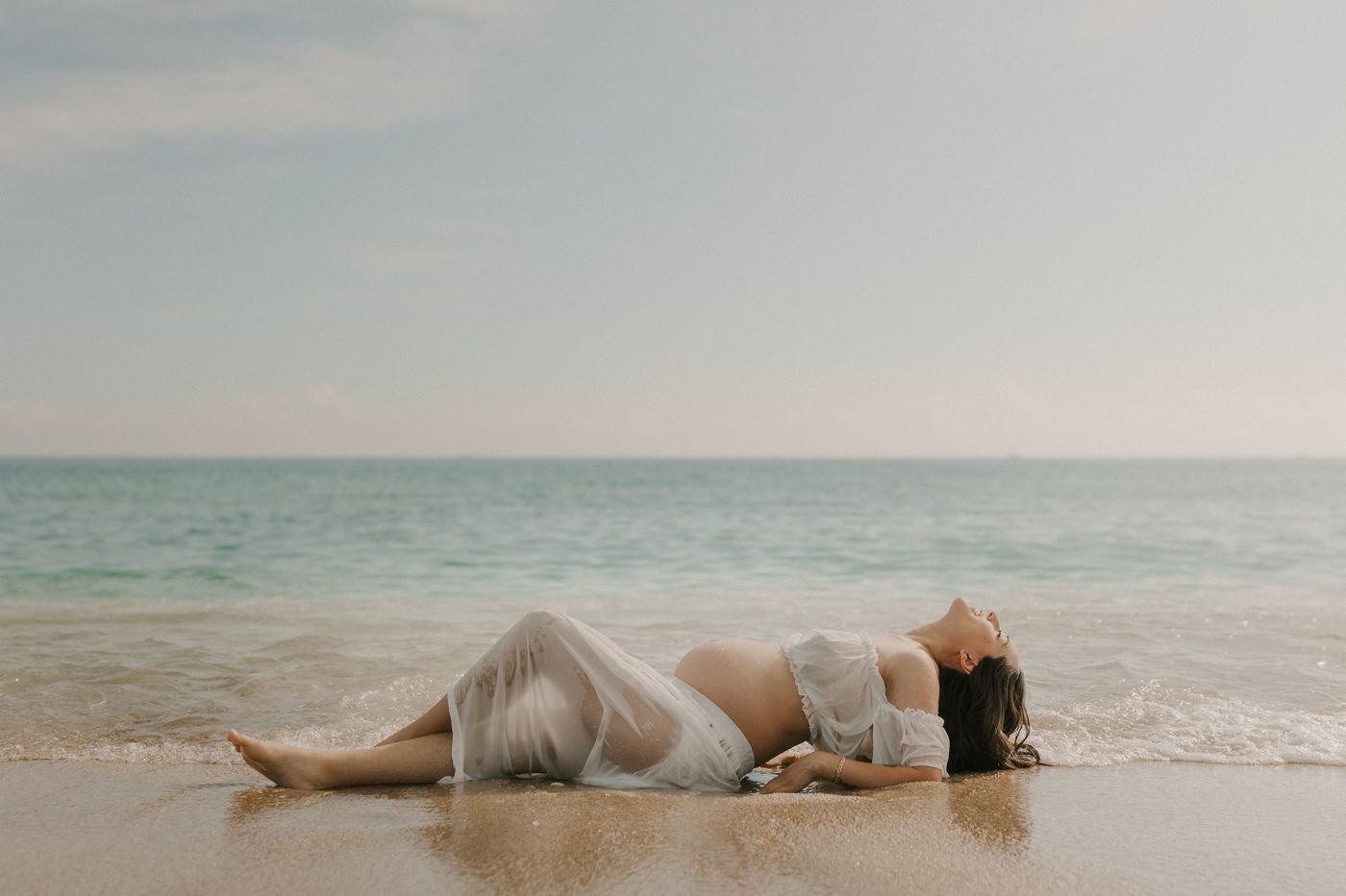 Femme enceinte en robe blanche profitant d’un moment calme au bord de la mer