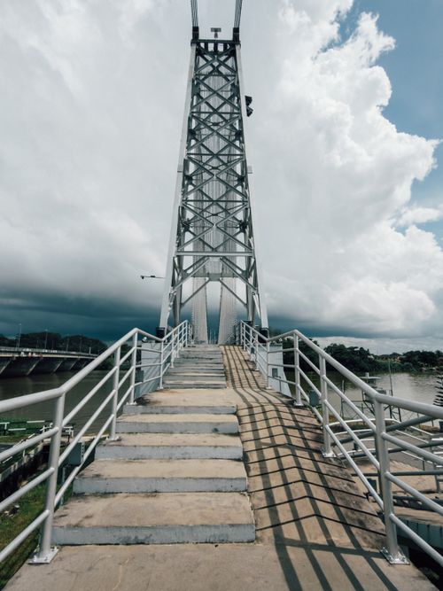 Free Dramatic view of a steel suspension bridge with looming clouds in the background. Stock Photo