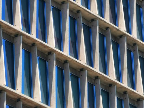Free Close-up of a modern building facade with blue-tinted windows and structural beams. Stock Photo