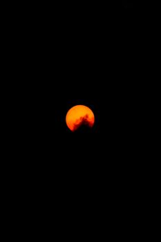 Captivating view of the orange moon setting in the dark night sky, creating a dramatic celestial scene.