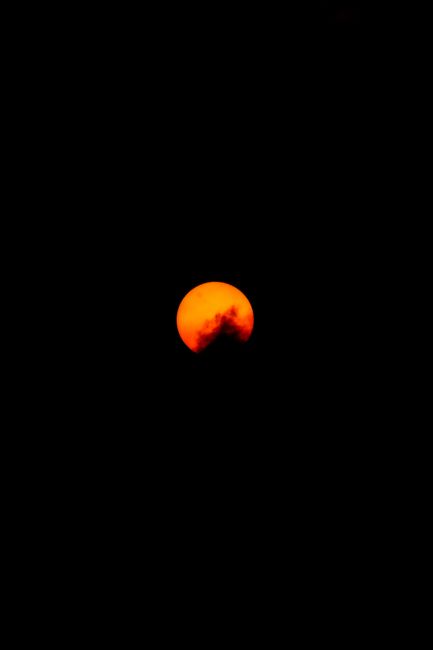 Captivating view of the orange moon setting in the dark night sky, creating a dramatic celestial scene.