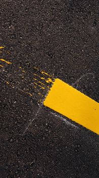 Detailed view of a freshly painted yellow line on a textured asphalt road surface.