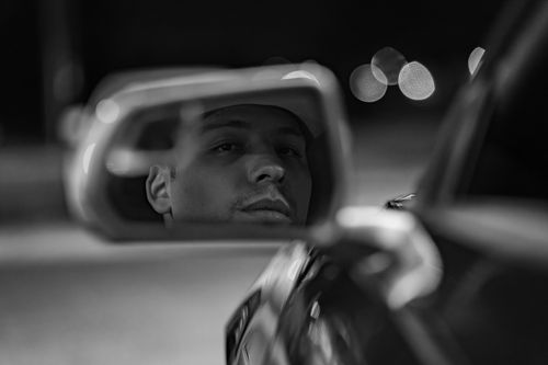 Free Black and white photo of a man reflecting thoughtfully in a car's rearview mirror. Stock Photo
