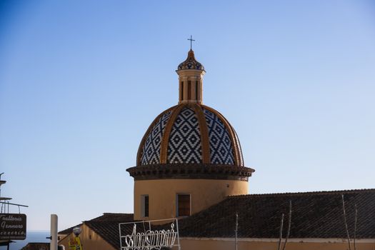 Colorful tiled dome of a Mediterranean church under clear blue skies in Italy.