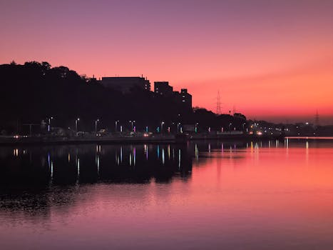 Beautiful sunrise with pink hues and silhouettes of buildings and trees reflected over calm water in Bhopal, India.