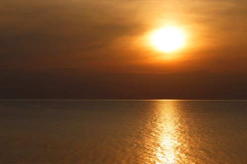 Free Dramatic sunset over the calm ocean, casting golden reflections on the water. Stock Photo