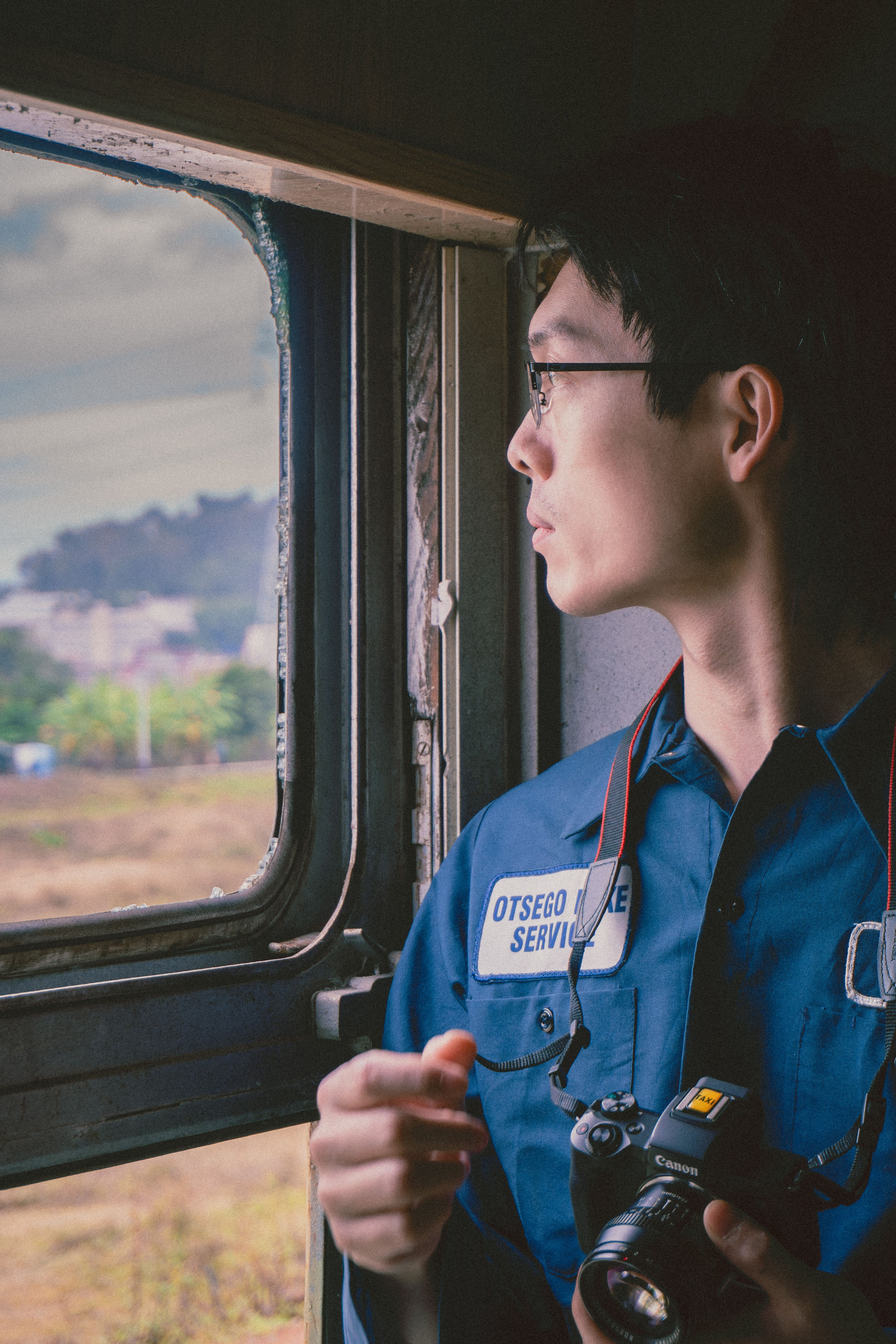 A person looks out a train window, camera in hand, contemplating the scenic view.