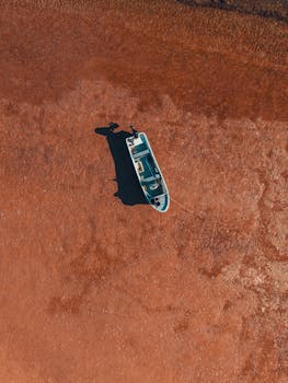 Aerial shot of a lone boat on a muddy beach in Olhão, Portugal, highlighting serene coastal beauty.