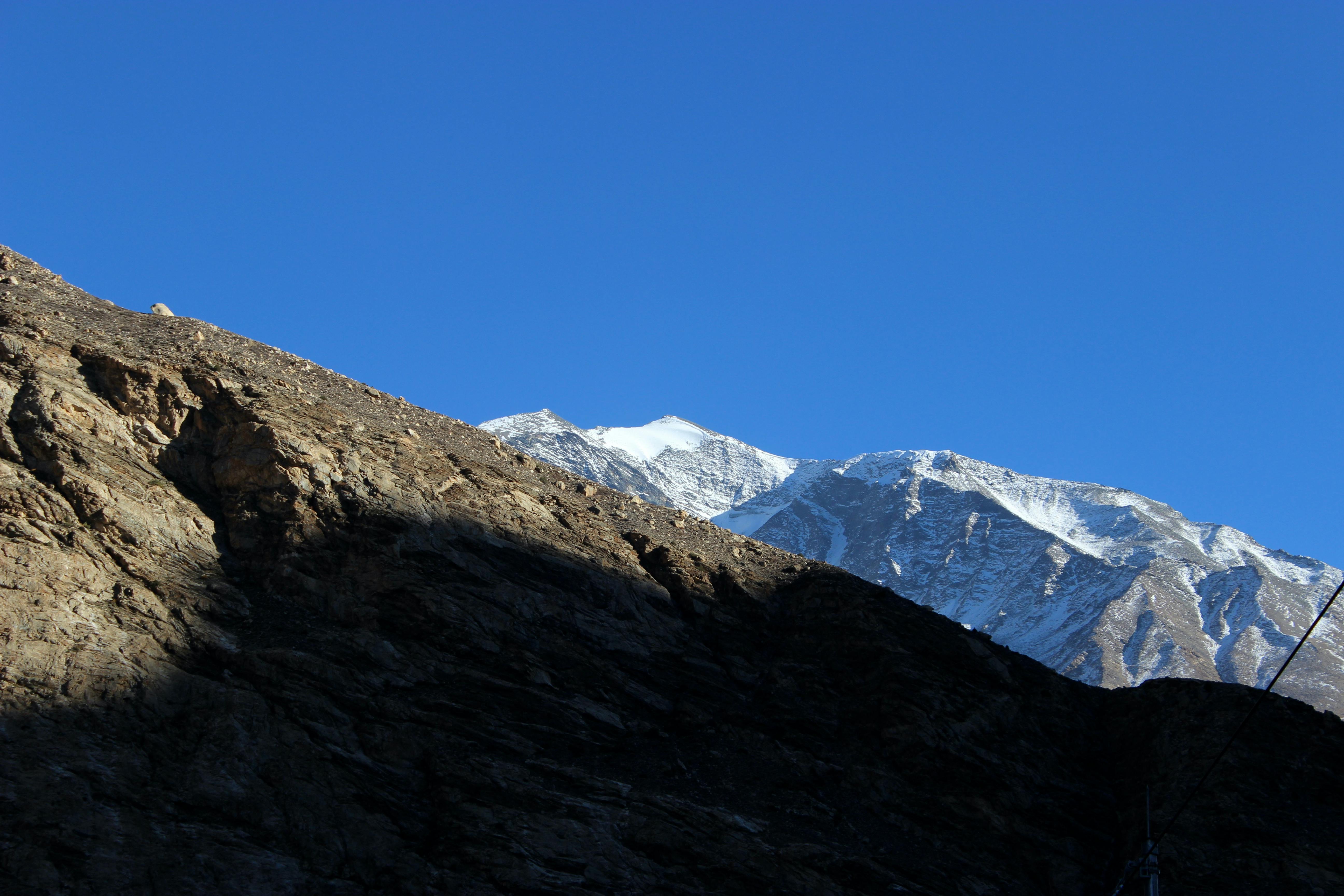Majestic snow-covered mountain peak with rocky foreground against a clear blue sky.
