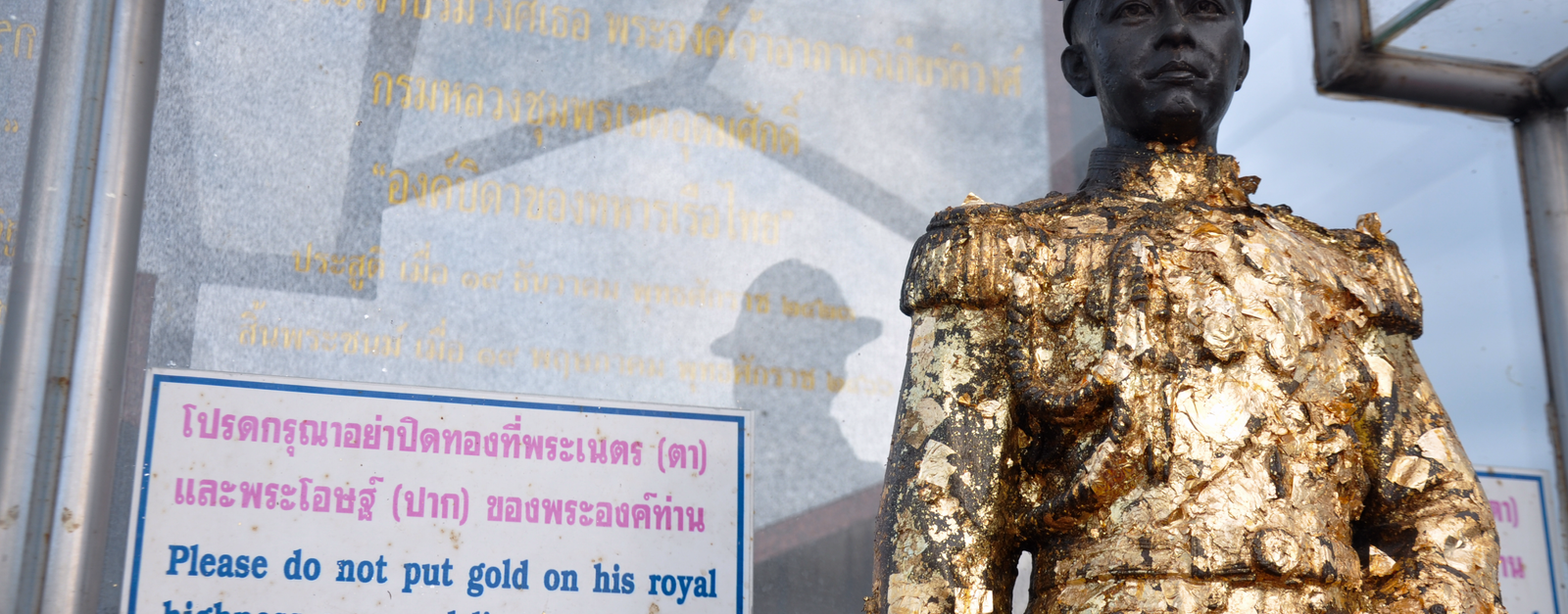 Golden statue in Thailand with sign requesting not to cover eyes and lips. Cultural respect imagery.