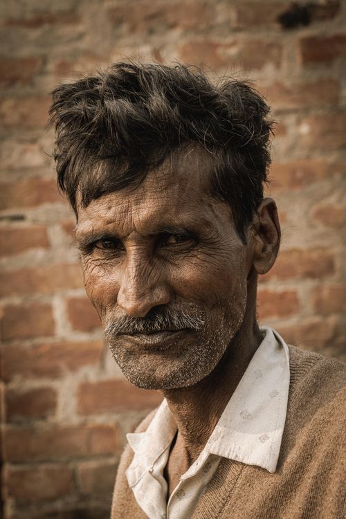 Free Close-up portrait of an elderly man with expressive wrinkles against a rustic brick wall. Stock Photo