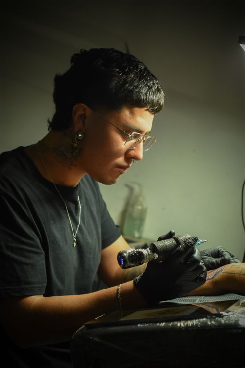 Free Tattoo artist concentrating on inking design in studio with precision. Stock Photo