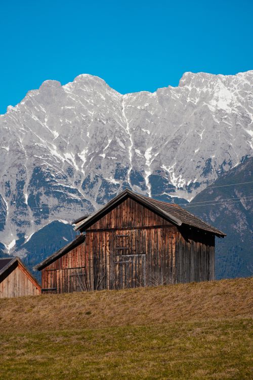 Free A picturesque wooden cabin set against the stunning Tyrolean Alps backdrop under a clear blue sky. Stock Photo