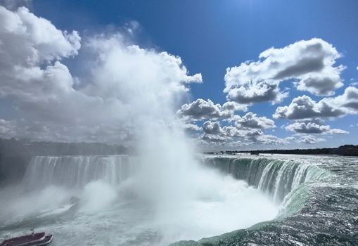 Breathtaking capture of Niagara Falls with mist and a vibrant blue sky. Ideal for nature and travel enthusiasts.