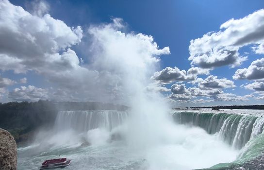 Dramatic view of Niagara Falls with clouds and a boat in the foreground. Perfect for travel promotions.