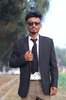 Young man in a suit and sunglasses posing confidently in an outdoor setting.