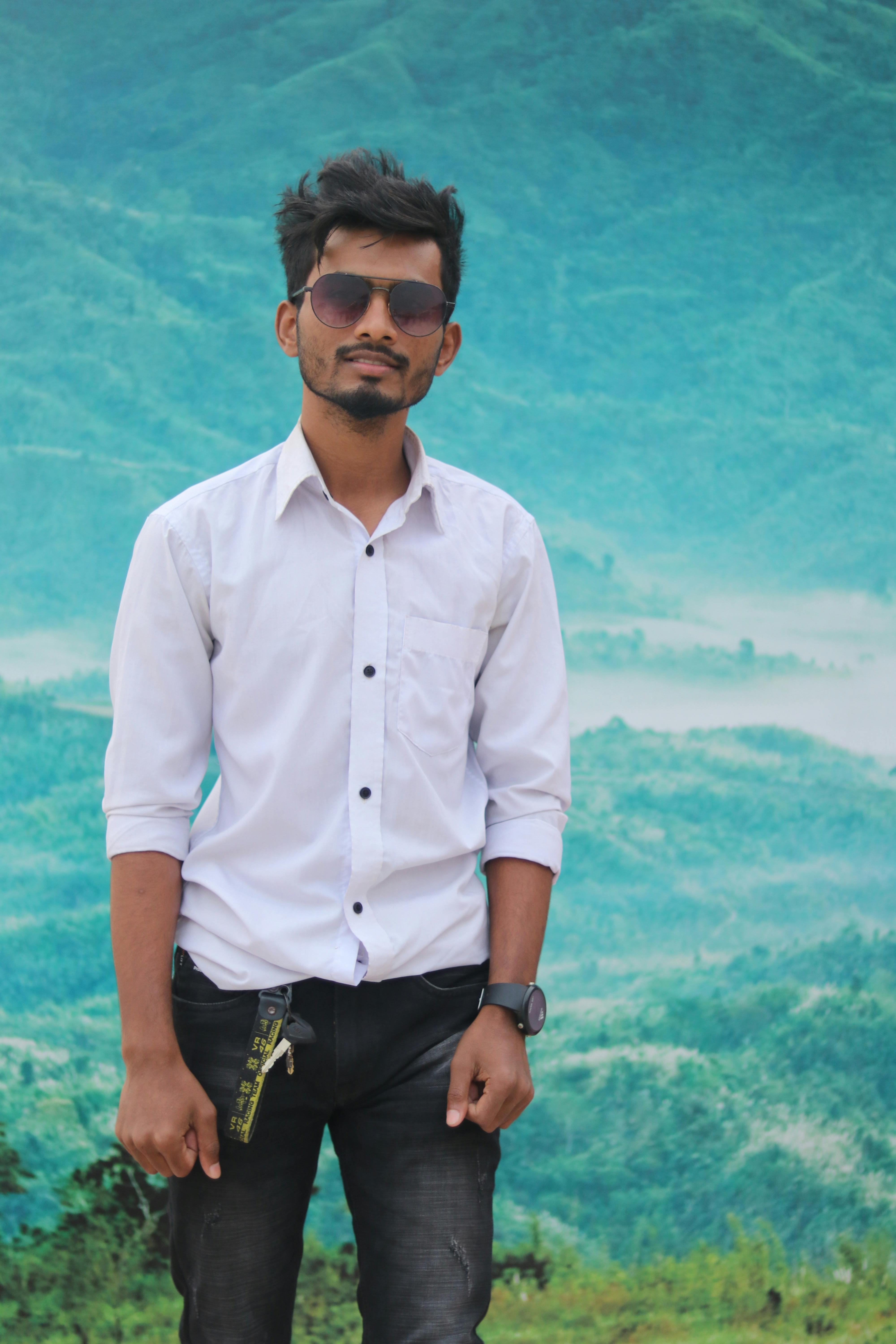 A young man in sunglasses poses confidently with a scenic mountain backdrop, exuding modern style.