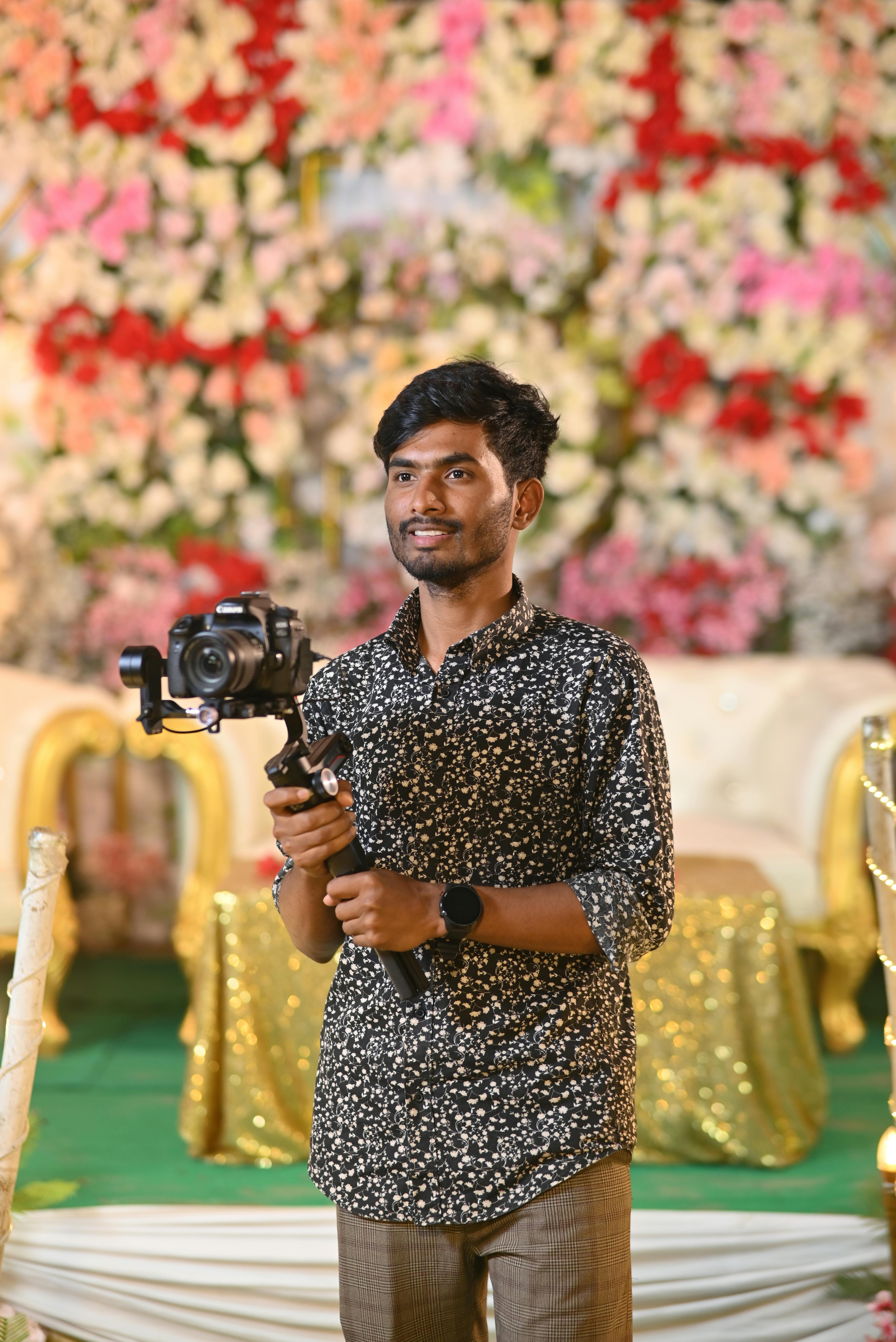 ฟรี ช่างภาพยิ้มแย้มขณะถือกล้องในสถานที่ที่ตกแต่งด้วยดอกไม้ คลังภาพถ่าย