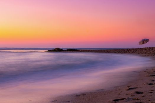 Vibrant beach sunset with umbrella and calm waves in a serene setting.